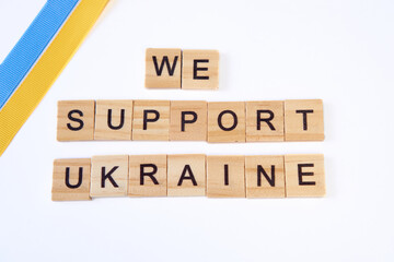 phrase we support ukraine is laid out of wooden squares isolated on white background. with flag of ukraine with blue and yellow ribbon. Concept of peace, war in Ukraine