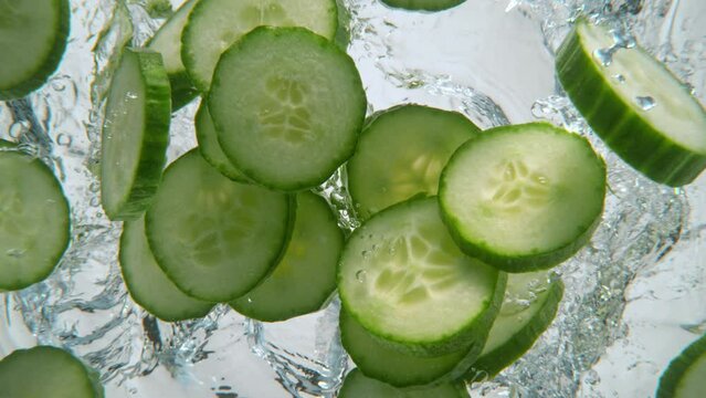 Super slow motion shot of falling pieces of cucumber into water, white background. Filmed on high speed cinematic camera at 1000 fps.