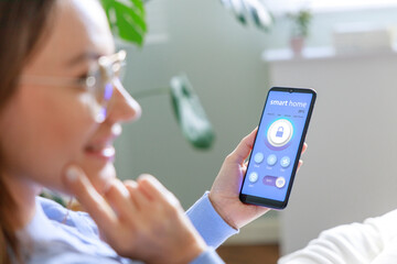 Young woman holding a smartphone with smart home screen