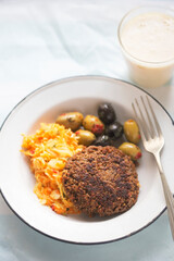 Vegetable burger with sunflower seeds, olives and raw vegetable salad with banana smoothie