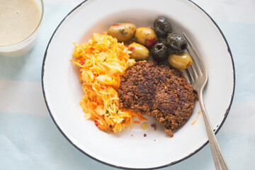 Vegetable burger with sunflower seeds, olives and raw vegetable salad with banana smoothie