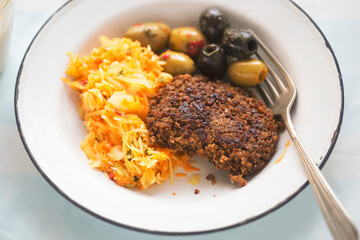 Vegetable burger with sunflower seeds, olives and raw vegetable salad with banana smoothie