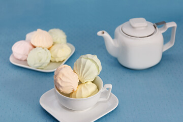  On a serviced table with a blue tablecloth lies a stunning fresh marshmallow and a teapot with fragrant tea