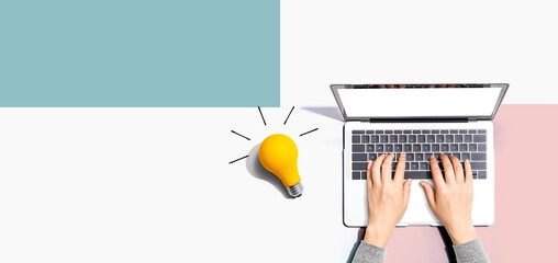 Person using a laptop computer and a light bulb - Flat lay