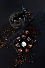 Dark chocolate candies in the assortment. An old coffee bean mill. Candy on a black stone board. Vertical photo.A cup of coffee. Dessert for the holiday. Black background.Flat lay.