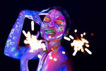 Woman with sparkler in neon light. Beautiful model girl colorful bright fluorescent makeup. Holiday...