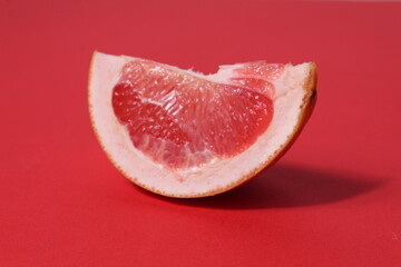 a piece of a slice of red grapefruit on a red background with a hard shadow. Fruit creative benefit...