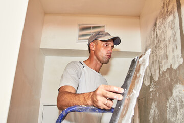 The master with a spatula is preparing to putty the surface of the wall for fixing the walls and preparing for painting.