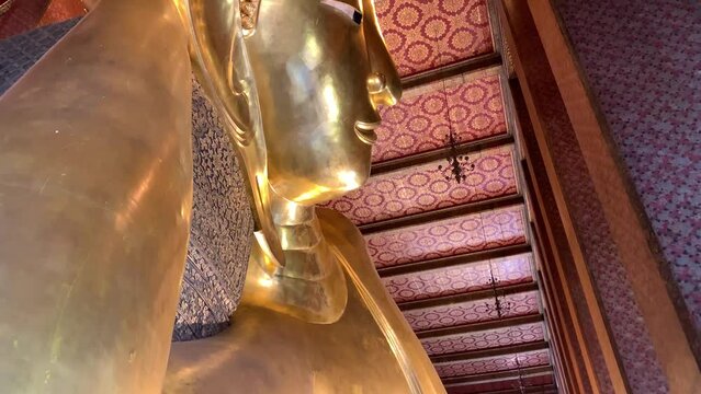 BANGKOK, THAILAND - Circa November, 2021: Golden Reclining Buddha Statue at Wat Pho, world heritage buddhist temple. This sleeping posture known as sihasaiyas. Beautiful background wall - Tilt up shot