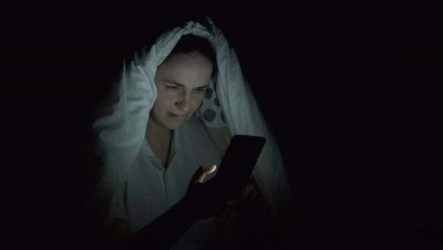 Young Woman Under Blanket Using Smartphone in Bed at Night, News and Social Media Addiction. Insomnia and Sleep Disorder Concept