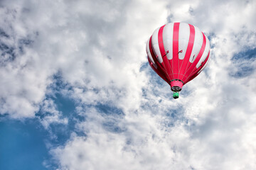 Red and white hot air balloon on background of bright blue cloudy sky.