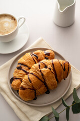 Croissants with chocolate and coffee cup on bright background. Breakfast time