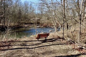 The empty park bench near the creek in the woods.