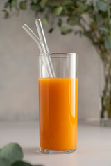Orange juice glass with reusable glass straws, on bright background