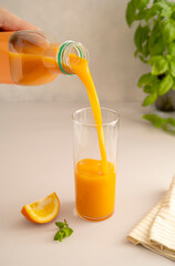 Orange juice pouring from plastic bottle in glass, isolated on bright background