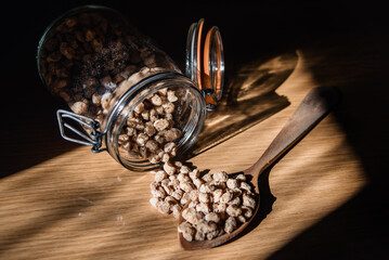 Cucharón de madera lleno de granos de soja texturizada gruesa junto a un tarro de cristal volcado...