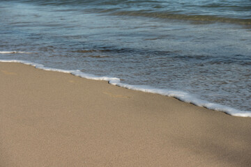 Fototapeta na wymiar Ocean's foam and wet sand. Close up on a wave and sandy beach. 