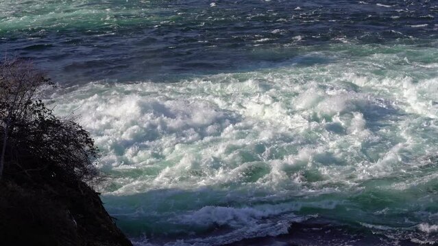 Close-up of famous Rhine Falls in backlight with splashing water flowing into natural pool on a sunny spring day. Movie shot March 5th, 2022, Zurich, Switzerland.