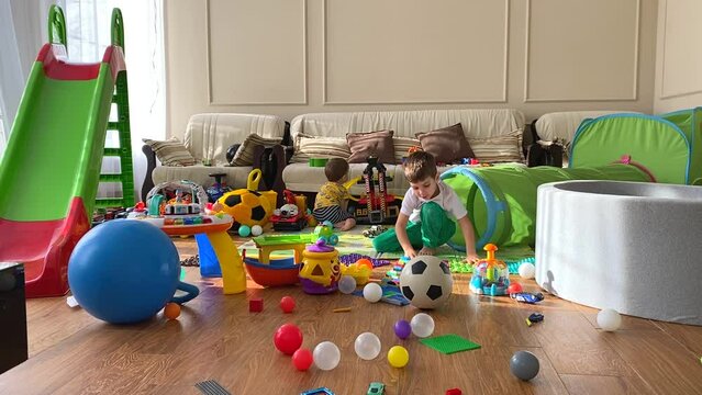 Two cute children are playing with toys in the children's room. A mess in the children's room. Children among scattered toys