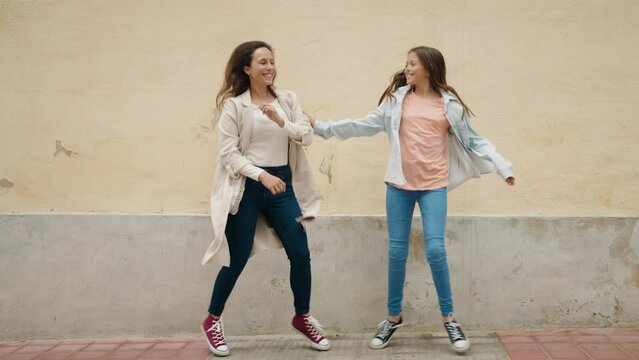 Mother and daughter smiling confident dancing at street