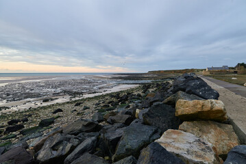 Rocky shore ay sunset. Stones, algae. Dramatic sky. D-Day landing beach view in Normandy, France....