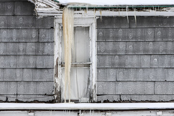 Old asbestos shingle siding on a house in winter with icicles from an ice dam