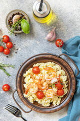 Mediterranean cuisine, seafood diet. Italian creste di gallo pasta with grilled prawns and tomatoes on a stone tabletop. Top view flat lay.