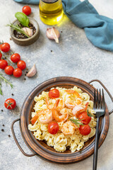 Mediterranean cuisine, seafood diet. Italian creste di gallo pasta with grilled prawns and tomatoes on a stone tabletop. Copy space.