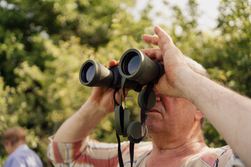 Senior man looking through a binocular among many green trees