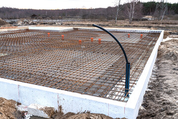 The foundation slab is made of reinforcement rods, bound with tie wire, visible sewage pipes and a...