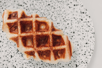 Close up small piece of homemade waffle on white dots dish.