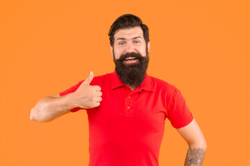 Fototapeta premium happy bearded man with moustache in tshirt showing thumb up on orange background, haircut