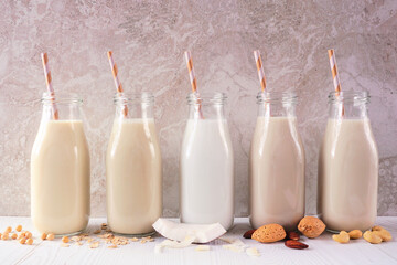 Assortment of vegan, plant based, non dairy milks in bottles. Side view with scattered ingredients...