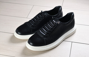 A pair of black sneakers with white soles on ceramic tiles. 