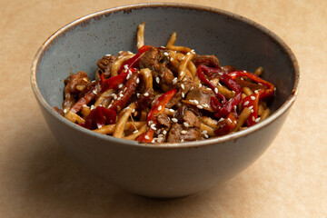 Wok with beef and red pepper in a plate on a brown background.