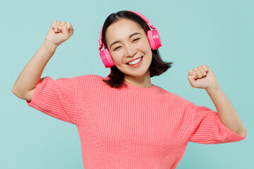 Young smiling happy woman of Asian ethnicity 20s wearing pink sweater headphones listen to music...