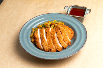 Fried chicken breast and fried potatoes in a plate on a brown background.