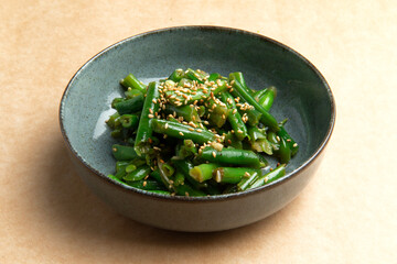 Cooked green beans in a plate on a brown background.