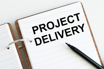 PROJECT DELIVERY inscription on the notebook on the table next to the black marker