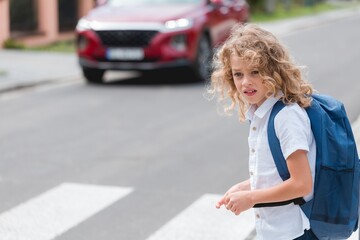 Cute little boy with a blue backpack crosses the street