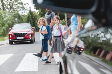 Group of school children goes through the pedestrian crossing in the street, right in front of the...