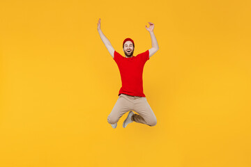 Obraz premium Full body fun excited delivery guy employee man in red cap T-shirt uniform workwear work as dealer courier jump high stretch hands isolated on plain yellow background studio portrait. Service concept.