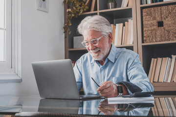 Happy old senior businessman looking at laptop screen and smiling on reading email sitting at home...