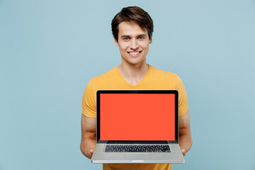 Young smiling man 20s wear yellow t-shirt hold use work on laptop pc computer with blank screen workspace area isolated on plain pastel light blue background studio portrait. People lifestyle concept.