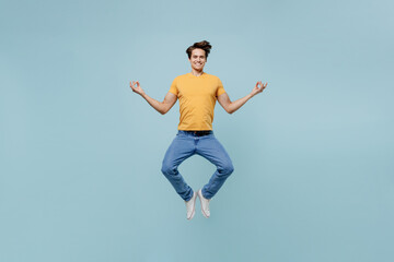 Full body spiritual young man wear yellow t-shirt jump high hold spreading hands in yoga om aum gesture relax meditate try to calm down isolated on plain pastel light blue background studio portrait