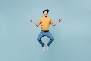 Fototapeta na wymiar Full body spiritual young man wear yellow t-shirt jump high hold spreading hands in yoga om aum gesture relax meditate try to calm down isolated on plain pastel light blue background studio portrait