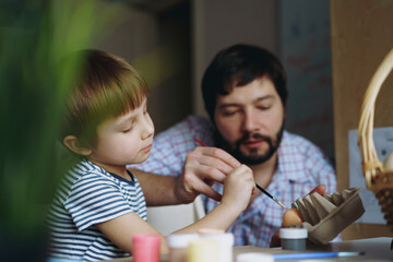 father and kid painting eggs for easter
