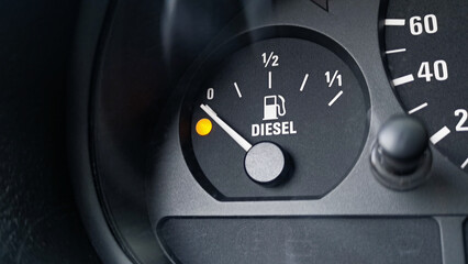 Close-up shot of a diesel fuel gauge in a car. Yellow light indicator and meter pointer showing that the tank is empty. Glare of light present on the gauge glass cover. Copy space