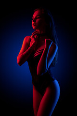 Beautiful young brunnete girl standing in sexy lingerie in colored light in studio on a dark background