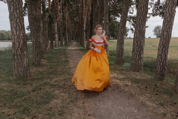 A young woman in an old orange dress walks on the shore of the lake near the castle